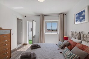 A bedroom with a bed, a dresser, a window with curtains, and a view of the outside. - Holiday Home 'Flôr' with Sea View, Private Terrace and Wi-Fi (Albufeira)