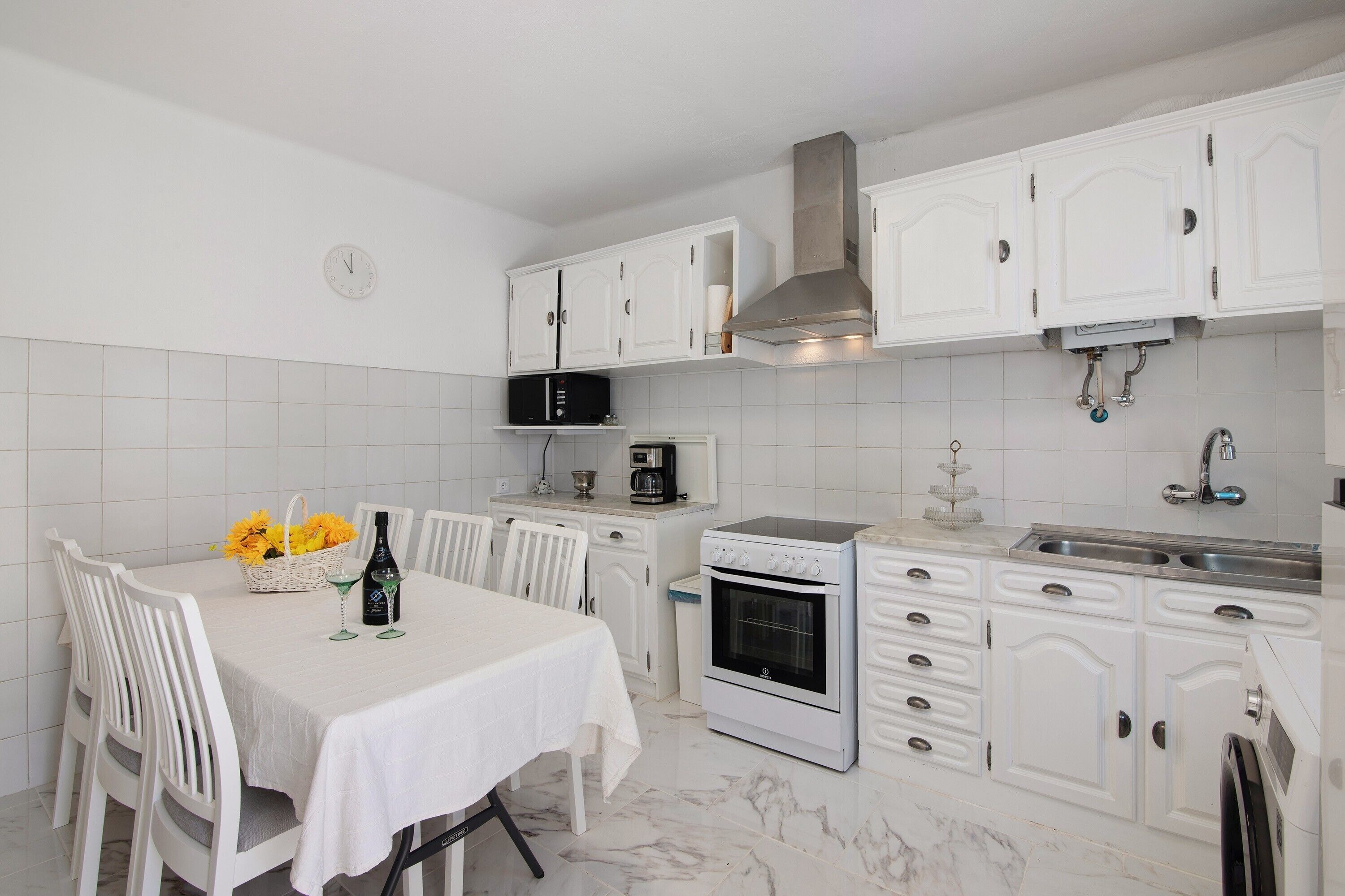 Cozinha com armários brancos, micro-ondas, forno e mesa de jantar com cadeiras.