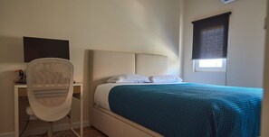 Une chambre à coucher comprenant un lit, un bureau, une chaise, une fenêtre avec un store et un téléviseur fixé au mur.