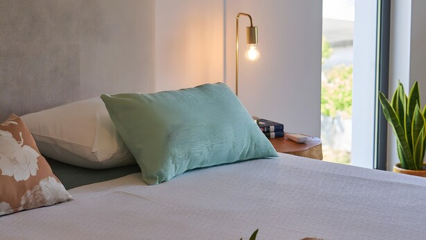 A neatly made bed with pillows, a bedside lamp, and rolled towels.