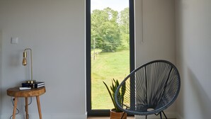 A room with a large sliding glass door, a black chair, a small wooden table with a lamp, and a potted plant.