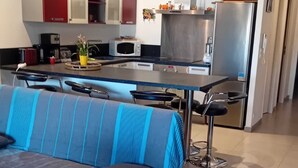 A modern living room with a blue-striped sofa, a wooden coffee table, and a kitchen area with a refrigerator, microwave, and red cabinets.