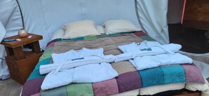 Een bed met een sprei, kussens en opgevouwen handdoeken in een tentachtige kamer.