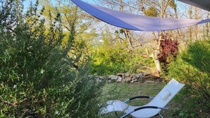 Un espace extérieur aménagé, abrité et doté de chaises et d’une table, entouré d’une végétation luxuriante et d’un mur en pierre.