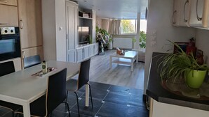 Une cuisine moderne avec un coin repas, un four encastré et une vue sur le salon.