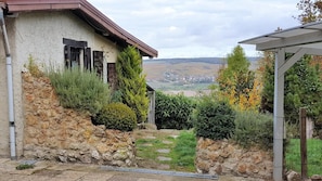 A rustic house with a stone wall, a wooden door, and a view of a valley.