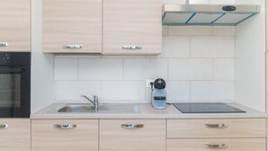 Una cocina moderna con armarios de madera clara, un lavamanos de acero inoxidable, un hervidor y un horno empotrado.