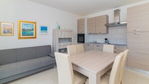 Una cocina moderna con armarios de madera clara, horno empotrado y comedor con mesa y sillas.