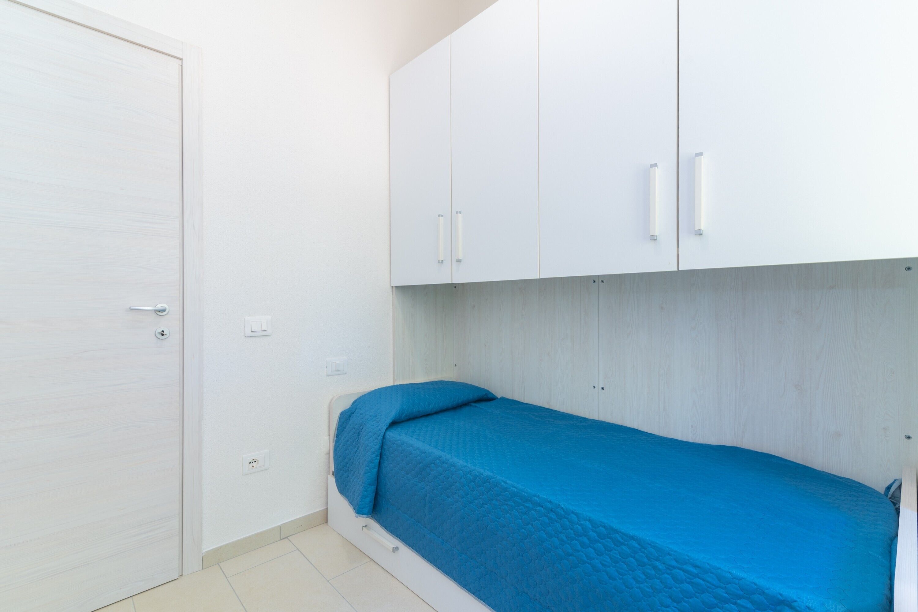 Ein kleines Zimmer mit einem Einzelbett, einem weißen Kleiderschrank und einer blauen Bettdecke.