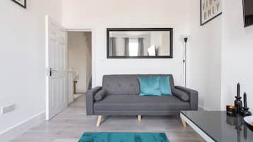 A modern living room with a grey sofa, teal rug, and a black table with candles.