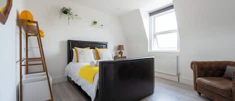 Une chambre avec un lit, une échelle, un canapé, une fenêtre et un radiateur.