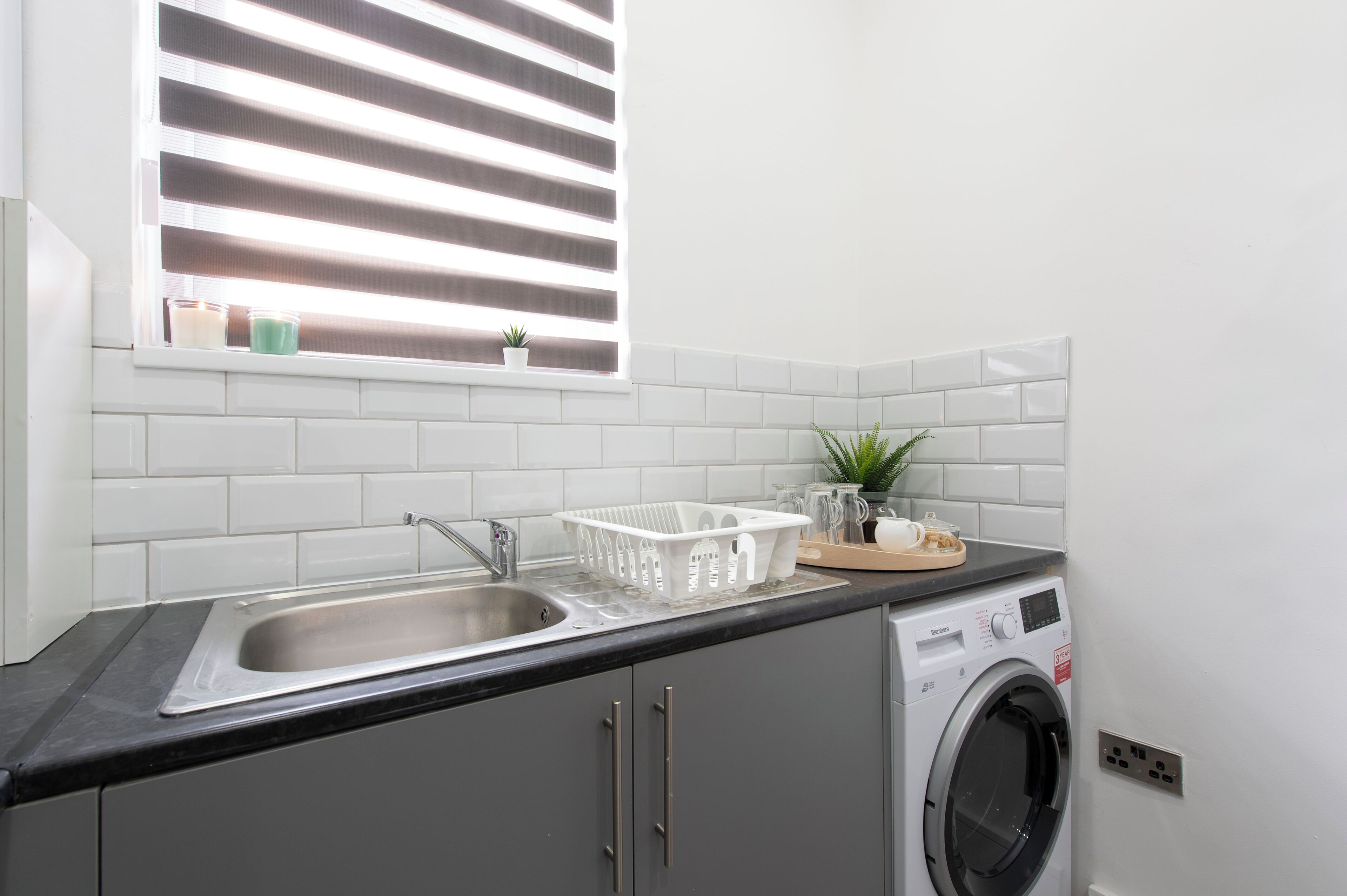 A kitchen with a sink, a washing machine, and a window with blinds.