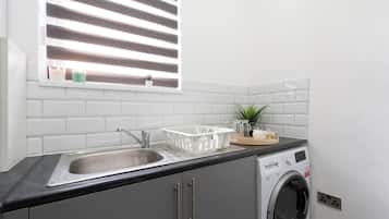 A kitchen with a sink, a washing machine, and a window with blinds.