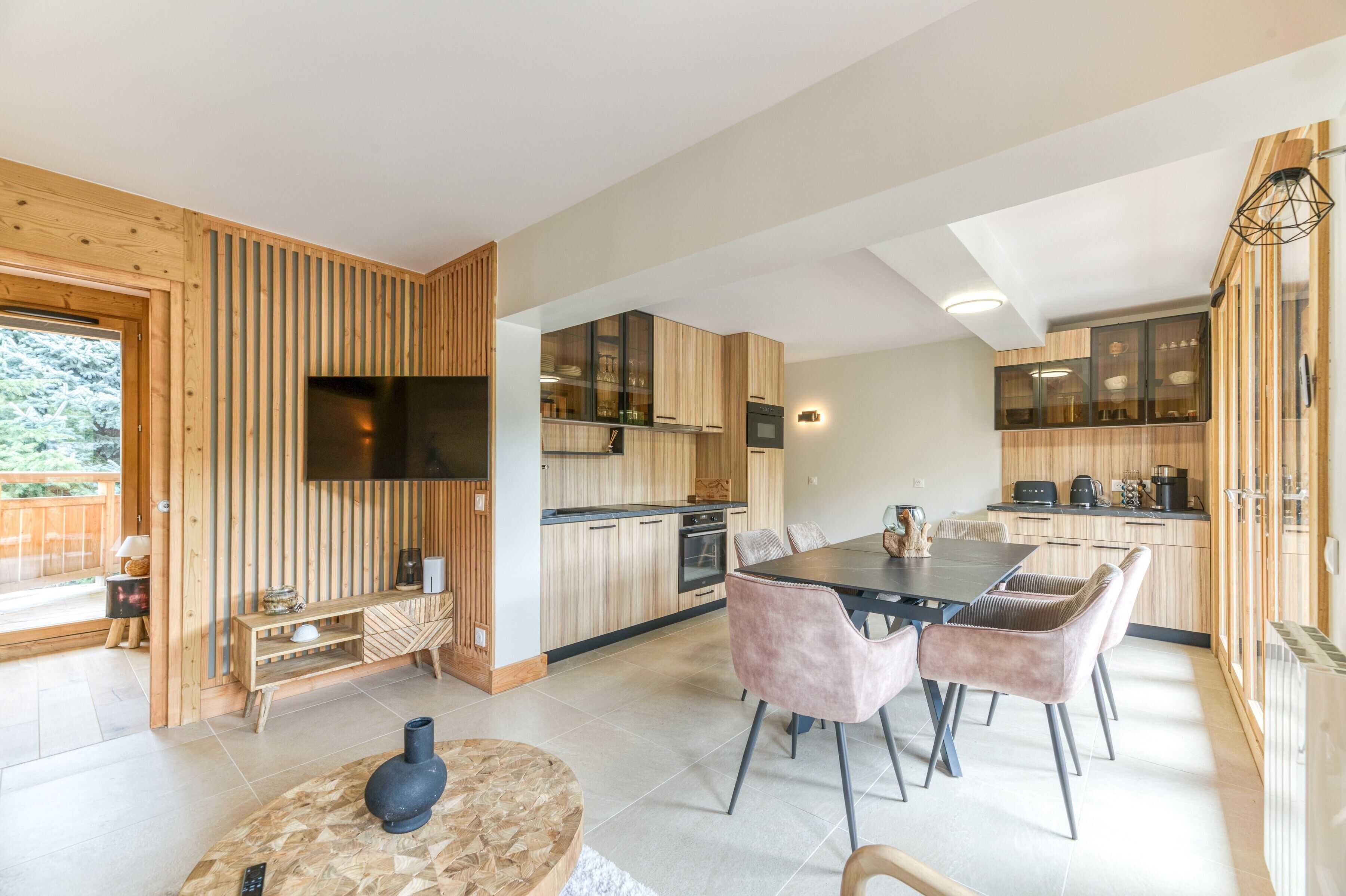 A modern kitchen with wooden cabinets, a dining area with a table and chairs, and a TV mounted on the wall.