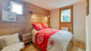 Un dormitorio con cabecera de madera, una ventana con vistas a árboles cubiertos de nieve, una cama con colcha roja y blanca, y un sofá blanco y mullido.
