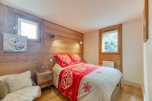 Une chambre à coucher avec une tête de lit en bois, une fenêtre donnant sur des arbres couverts de neige, un lit avec une couvre-lit rouge et blanc, et un canapé blanc moelleux.