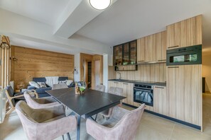 A modern kitchen with wooden cabinetry, a built-in oven, and a dining area with a black table and cushioned chairs.