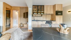 Una cocina moderna con armarios de madera, un comedor con mesa de mármol y un baño con ducha a la vista.