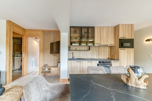 Une cuisine moderne avec des meubles en bois, un coin repas doté d’une table en marbre et une salle de bain ouverte avec douche.