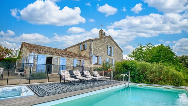 A swimming pool with lounge chairs, a stone building with blue shutters, and a clear sky.
