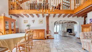 A spacious living area with a dining table, chairs, a sofa, a staircase, and a kitchen in the background.