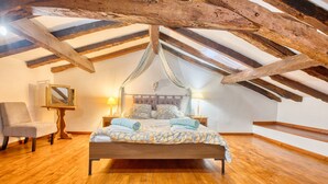 Une chambre avec un plafond en bois, un lit recouvert d’une couvre-lit à motifs, une chaise et des lampes de chevet.