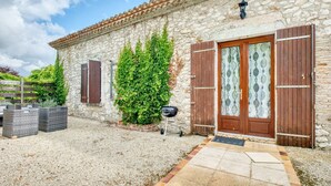 Un bâtiment en pierre avec un toit en tuiles, une porte en bois dotée de panneaux de verre et une allée gravillonnée.