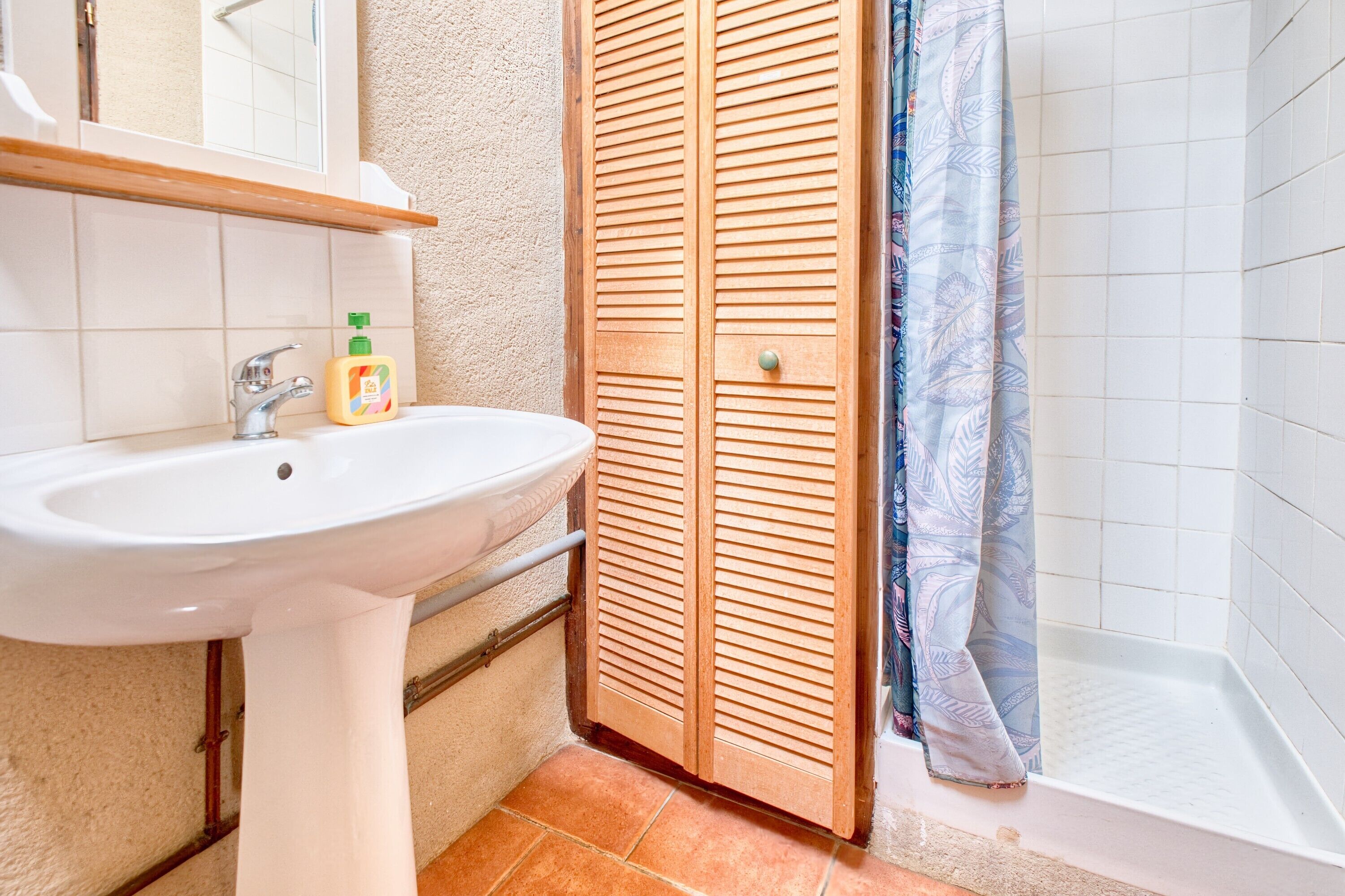 A bathroom with a white sink, wooden door, and a shower area.