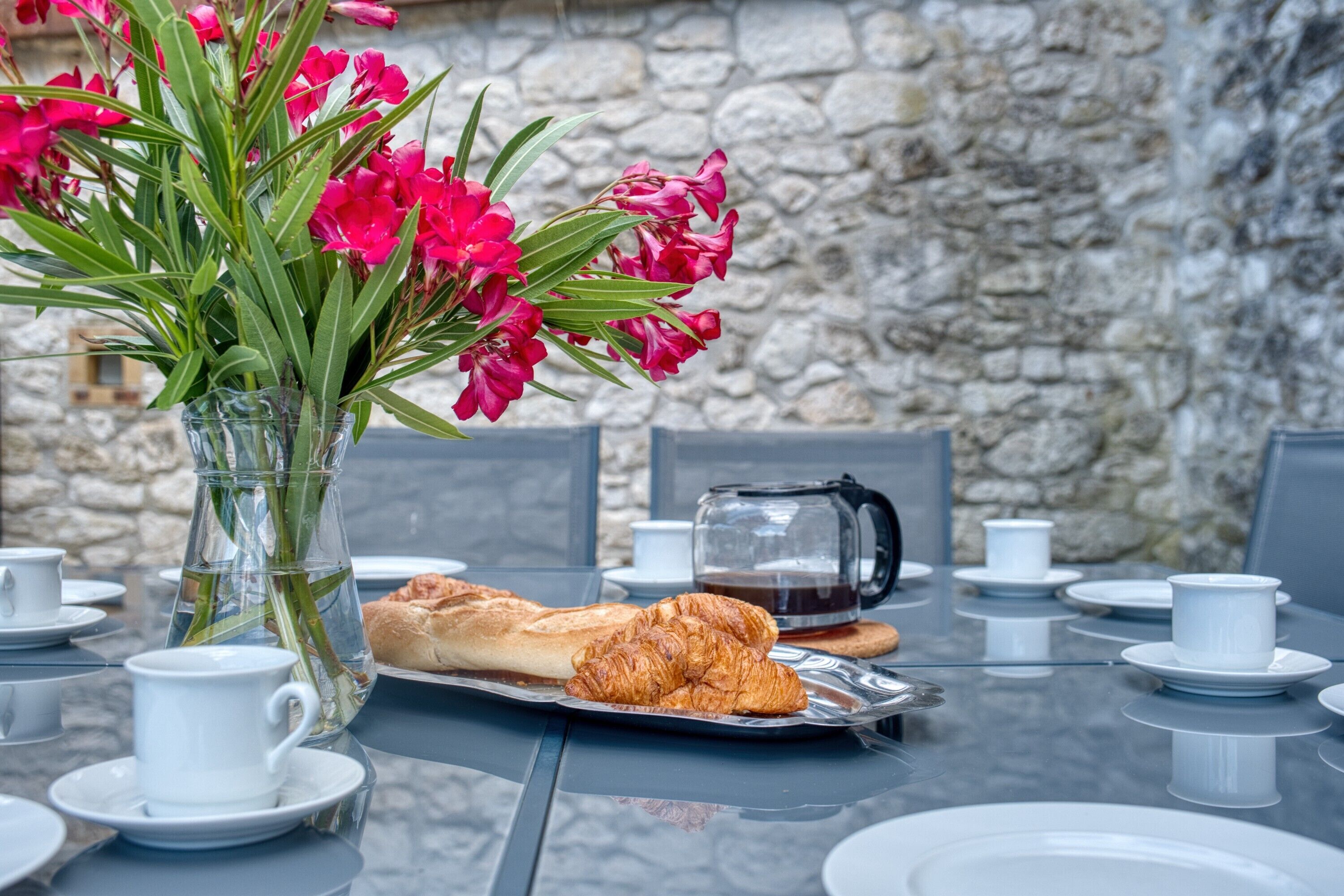 A table set with plates, cups, a tray with croissants, a vase with flowers, and a coffee pot.