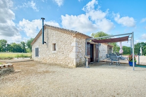 Un bâtiment en pierre doté d’une terrasse en gravier, d’une pergola et de mobilier d’extérieur.