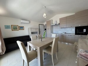 A modern kitchen with a dining area, a black sofa, and artwork on the wall. - Apartment 'Trilocale' with Sea View, Private Terrace and Air Conditioning (OLBIA)