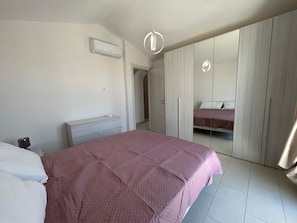A bedroom with a bed, bedside table, wardrobe, and an air conditioning unit.