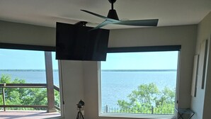 Un dormitorio con una cama grande, un ventilador de techo y vistas al mar a través de amplias ventanas.
