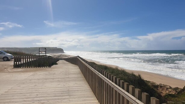 A wooden boardwalk leading to a beach with waves crashing onto the shore. - Villa 'Praia Azul Beach and Sun' with sea view, private garden, and Wi-Fi access (Silveira)