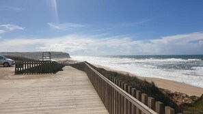 A wooden boardwalk leading to a beach with waves crashing onto the shore. - Villa 'Praia Azul Beach and Sun' with sea view, private garden, and Wi-Fi access (Silveira)