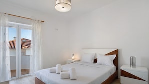 A bedroom with a bed, a nightstand, a lamp, and a view through a sliding door. - Villa 'Praia Azul Beach and Sun' with sea view, private garden, and Wi-Fi access (Silveira)