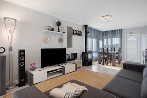 A modern living room with a flat-screen TV, a sofa, a coffee table, and a dining area with a table and chairs.