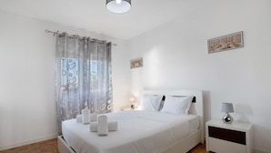 A neatly made bed with white linens and towels, a bedside table with a lamp, and a window with a sheer curtain. - Villa 'Praia Azul Beach and Sun' with sea view, private garden, and Wi-Fi access (Silveira)
