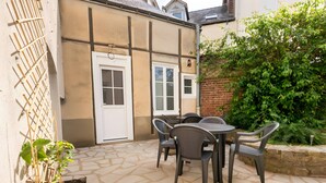 A patio with a table and chairs, a white door, and a brick wall with greenery. - Relax & Recharge: Elegant Home With Sauna (Le Mans)