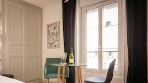 A hotel room with a bed, a table with two chairs, a bottle of champagne, and a window with curtains. - Relax & Recharge: Elegant Home With Sauna (Le Mans)