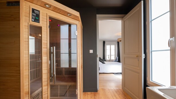A modern hotel room with a wooden sauna, a large window, and a view of the adjacent room. - Relax & Recharge: Elegant Home With Sauna (Le Mans)