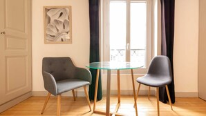 A room with a glass table and two chairs, a door, a framed abstract artwork, and a window with curtains. - Relax & Recharge: Elegant Home With Sauna (Le Mans)