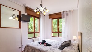 Una habitación de hotel con cama, televisor, candelabro y ventanas con cortinas.