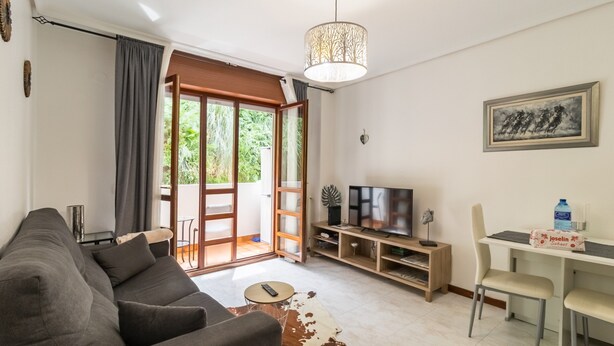 Una sala de estar con sofá, televisión y un comedor con sillas.