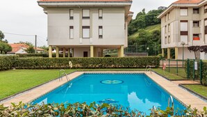 Una piscina con solárium alicatado, rodeada de césped cuidado y un edificio con tejado de tejas rojas.