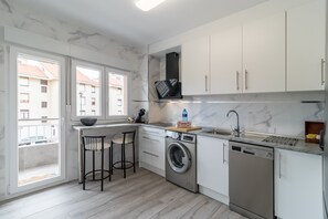 A modern kitchen with a washing machine, dishwasher, and a bar stool.