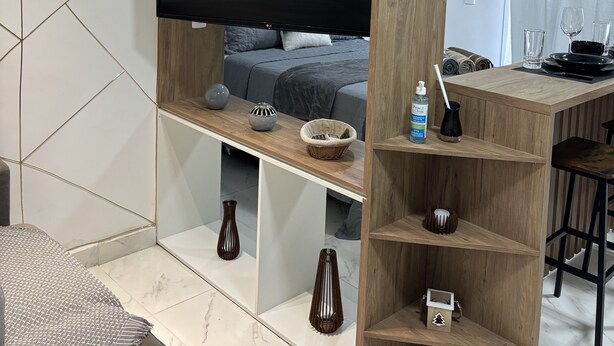 Un dormitorio moderno con un espejo grande, televisor, cama y zona de escritorio de madera con estanterías.