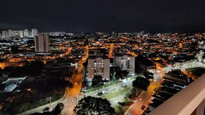 Un paisaje urbano nocturno con calles e edificios iluminados, un edificio central destacado y una vista desde un balcón.