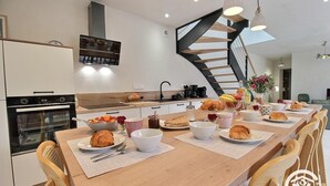 A modern kitchen with a wooden dining table set for breakfast, a built-in oven, and a spiral staircase.