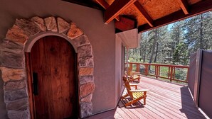 A wooden door with a stone archway, a wooden deck with chairs, and a view of a forest.
